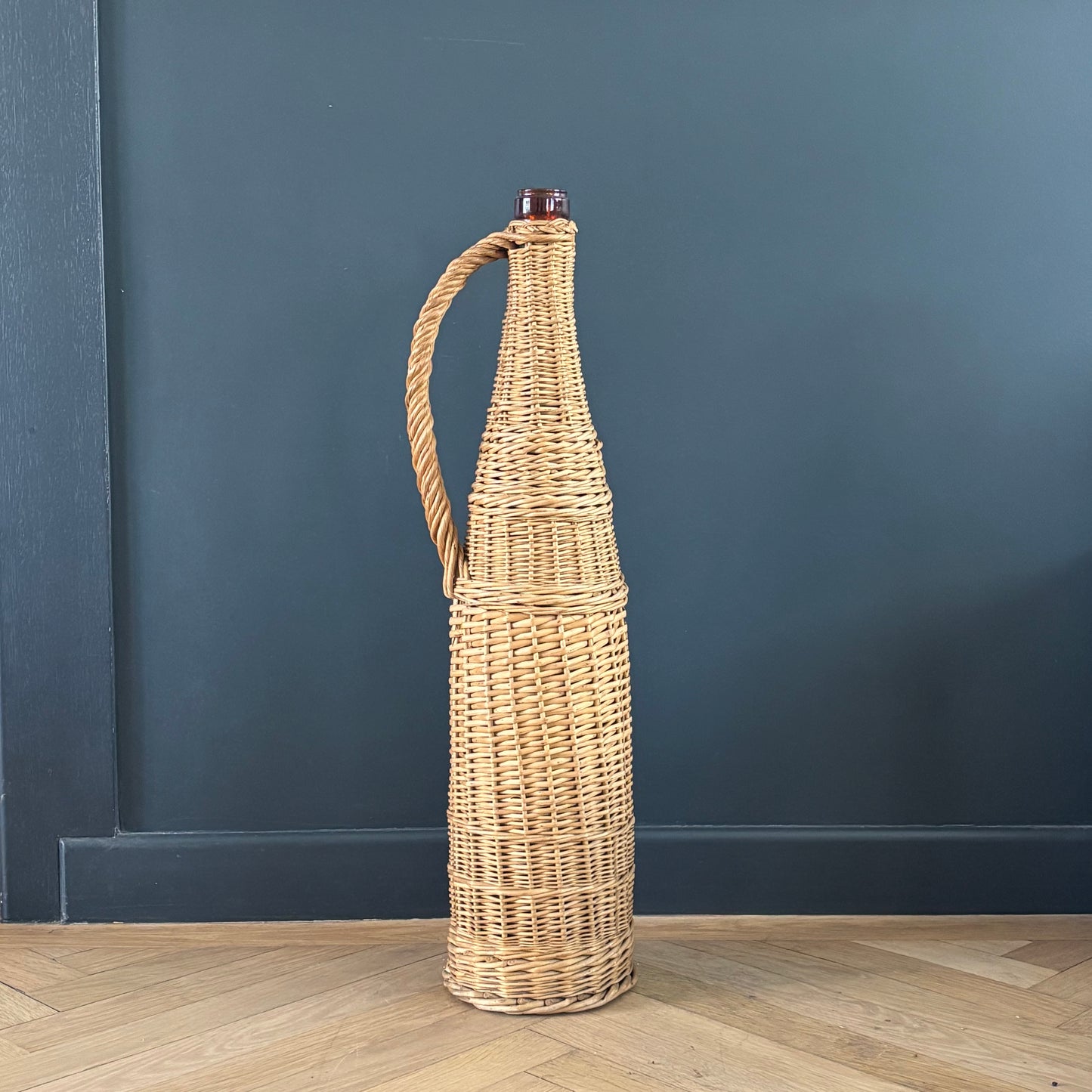 Bouteille en verre ambré dans son panier à poignée en osier - Ref 1232
