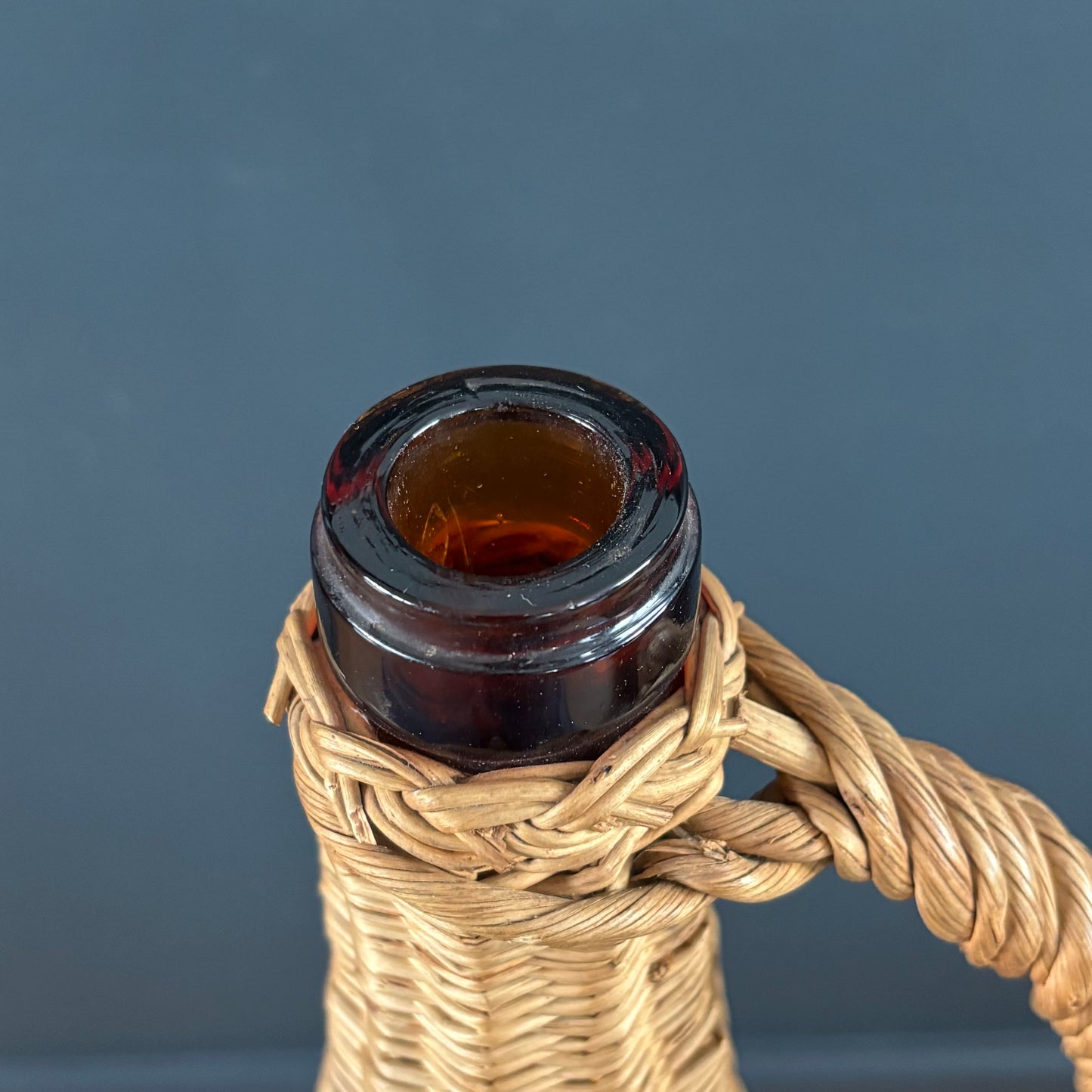 Bouteille en verre ambré dans son panier à poignée en osier - Ref 1232